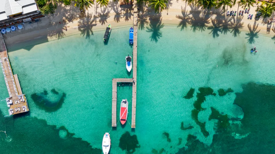 Aerial view of turquoise water, docks and palms along the Roatán shoreline